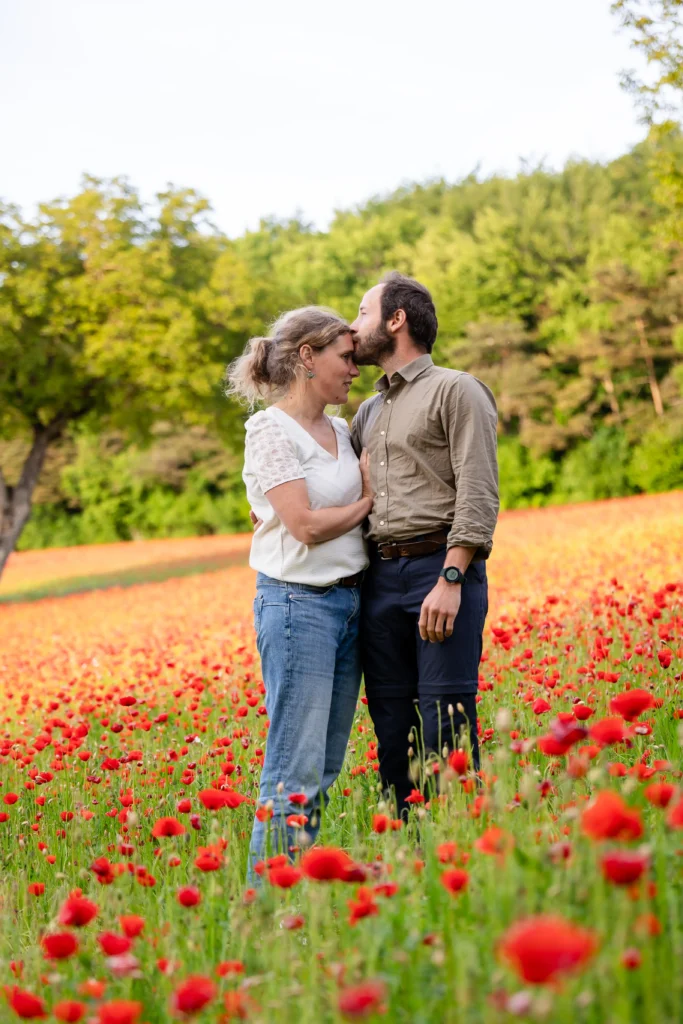 Couple enlacé dans un champ de coquelicots en Isère, séance engagement naturelle