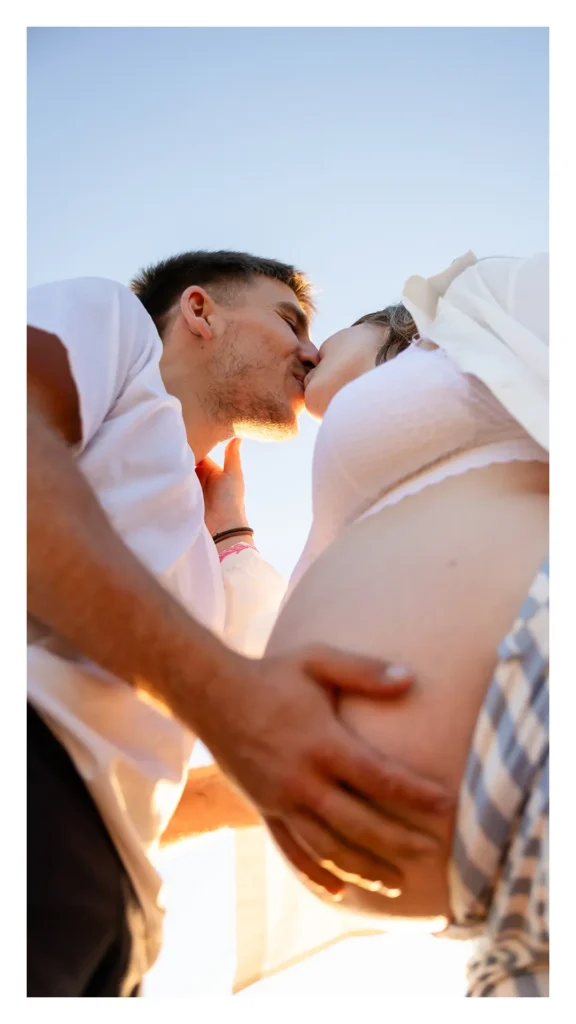 Mains des futurs parents posées sur le ventre de grossesse éclairé par la lumière dorée