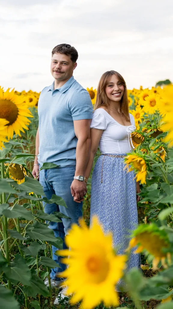 couple souriant au milieu d'un champ de tournesols se tenant la main